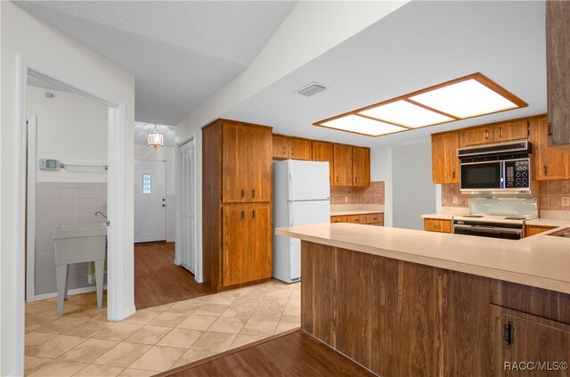 kitchen with stainless steel stove, light hardwood / wood-style floors, tasteful backsplash, decorative light fixtures, and white fridge