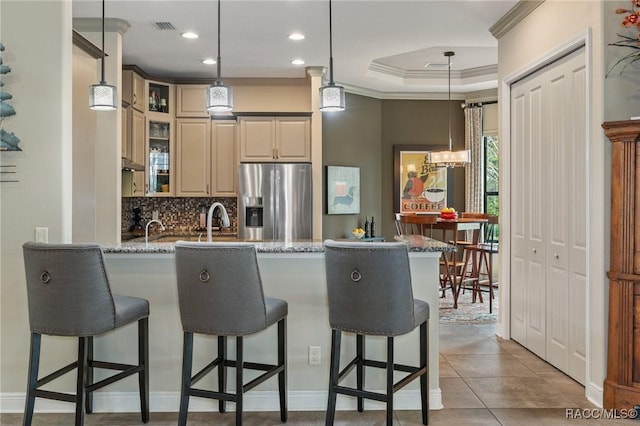 kitchen with hanging light fixtures, stainless steel fridge with ice dispenser, light stone counters, decorative backsplash, and a breakfast bar