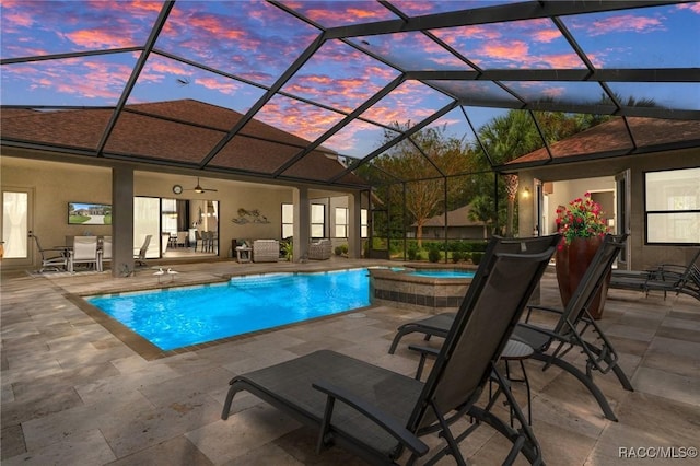 pool at dusk with glass enclosure, an in ground hot tub, and a patio