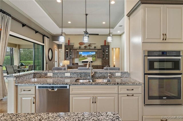 kitchen with pendant lighting, stainless steel appliances, a raised ceiling, and sink