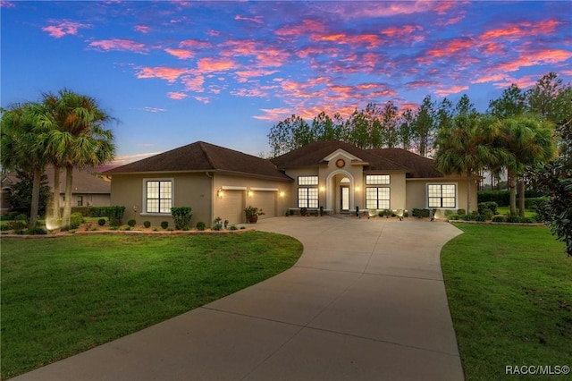 mediterranean / spanish home featuring a garage, driveway, a lawn, and stucco siding