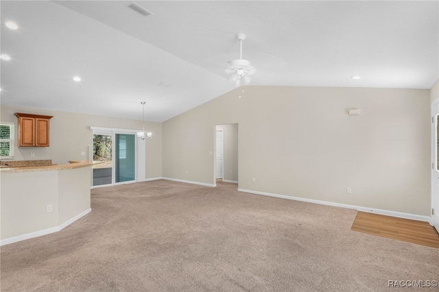 unfurnished living room with light carpet, ceiling fan with notable chandelier, and vaulted ceiling