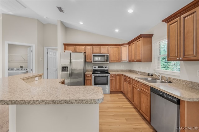 kitchen featuring washing machine and clothes dryer, sink, vaulted ceiling, appliances with stainless steel finishes, and light wood-type flooring