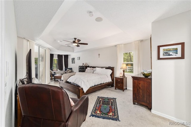 bedroom with ceiling fan, light colored carpet, a tray ceiling, and a textured ceiling