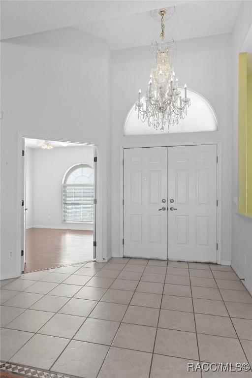 tiled entrance foyer featuring a towering ceiling and a notable chandelier