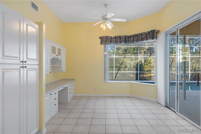 interior space with white cabinetry, ceiling fan, built in desk, and light tile patterned floors