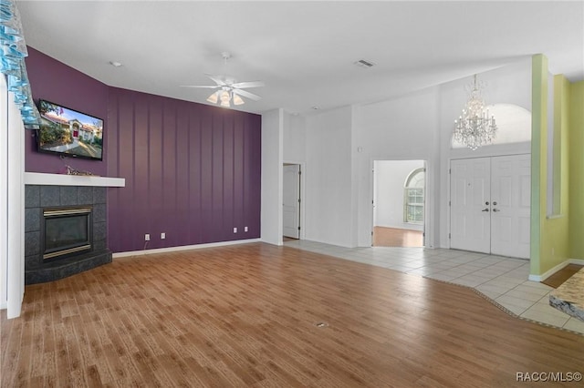 unfurnished living room with hardwood / wood-style floors, ceiling fan with notable chandelier, and a tile fireplace