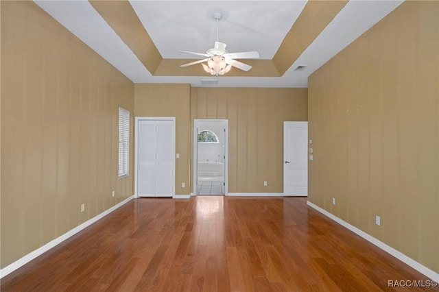 empty room with wood-type flooring, a tray ceiling, and ceiling fan