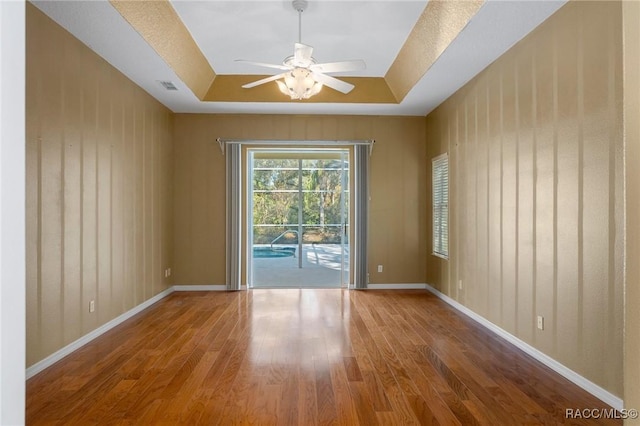 spare room with wood-type flooring, wood walls, ceiling fan, and a tray ceiling