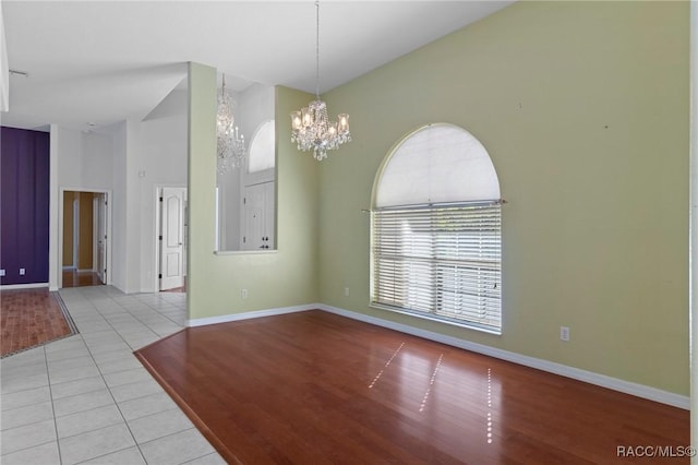 spare room with a towering ceiling, light hardwood / wood-style floors, and an inviting chandelier