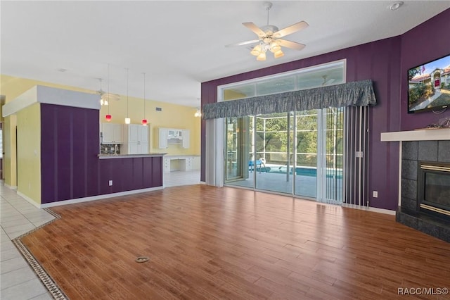 unfurnished living room with a tiled fireplace, ceiling fan, and light hardwood / wood-style flooring