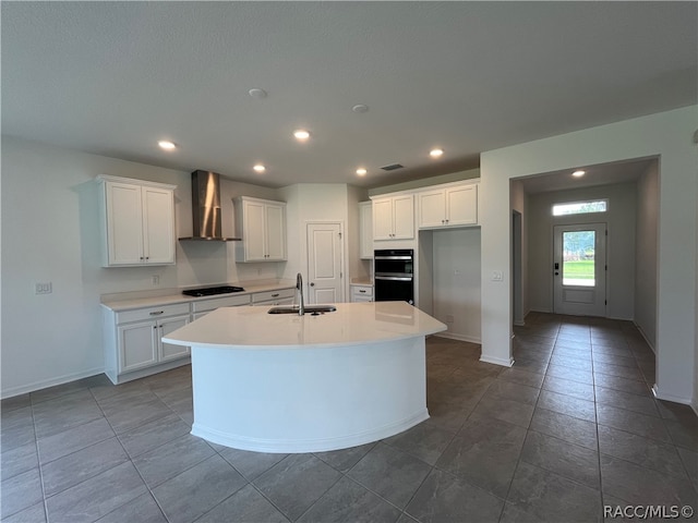 kitchen featuring wall chimney exhaust hood, white cabinetry, sink, and a kitchen island with sink