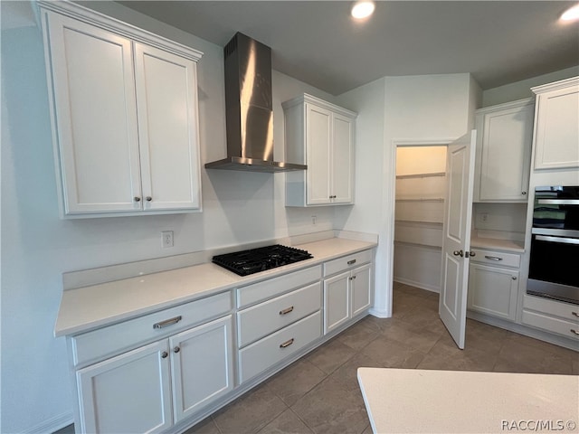 kitchen featuring white cabinetry, stainless steel double oven, wall chimney range hood, black gas stovetop, and light tile patterned floors