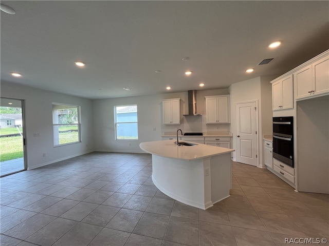 kitchen featuring white cabinetry, sink, wall chimney exhaust hood, an island with sink, and double wall oven