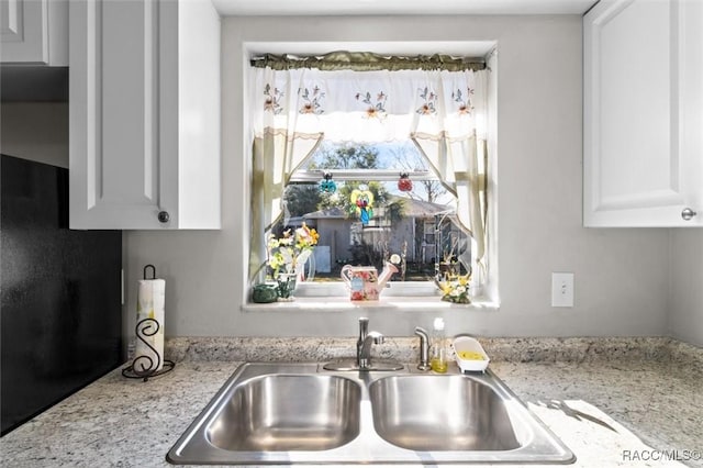 kitchen with light stone countertops, white cabinetry, and sink