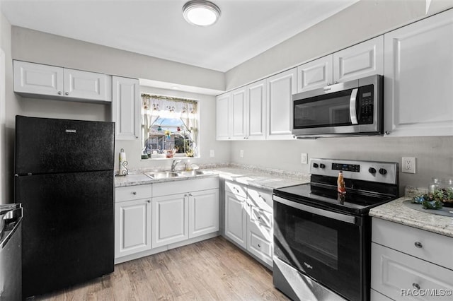 kitchen with light stone countertops, appliances with stainless steel finishes, sink, light hardwood / wood-style flooring, and white cabinetry