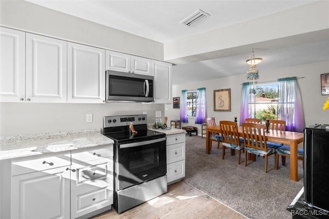 kitchen with white cabinetry, light colored carpet, light stone counters, and appliances with stainless steel finishes