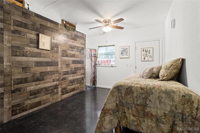 bedroom with ceiling fan, wood walls, and a textured ceiling