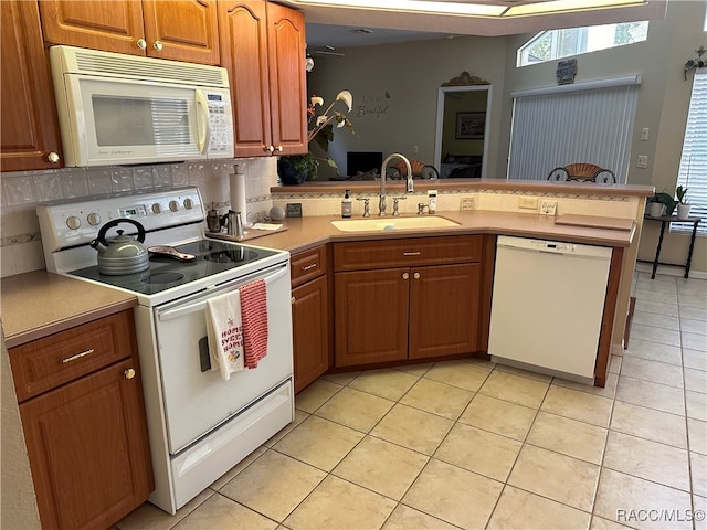 kitchen featuring light tile patterned flooring, white appliances, kitchen peninsula, and sink