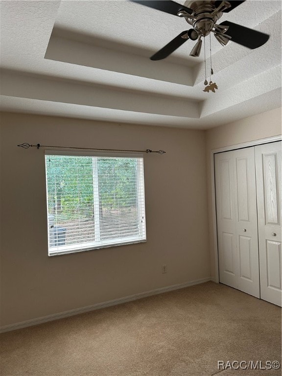 unfurnished bedroom with ceiling fan, a raised ceiling, a textured ceiling, light carpet, and a closet