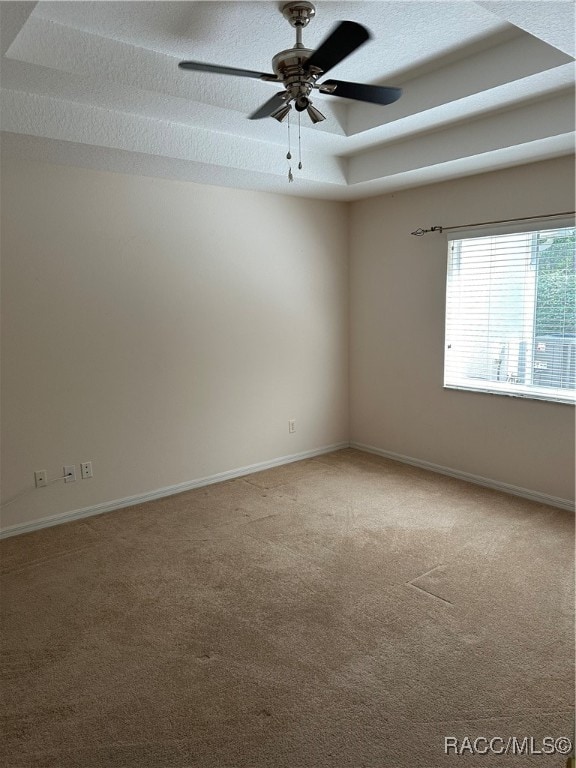 carpeted empty room featuring a textured ceiling, a raised ceiling, and ceiling fan