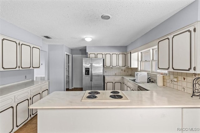 kitchen with stainless steel refrigerator with ice dispenser, kitchen peninsula, white electric cooktop, a textured ceiling, and light tile patterned floors