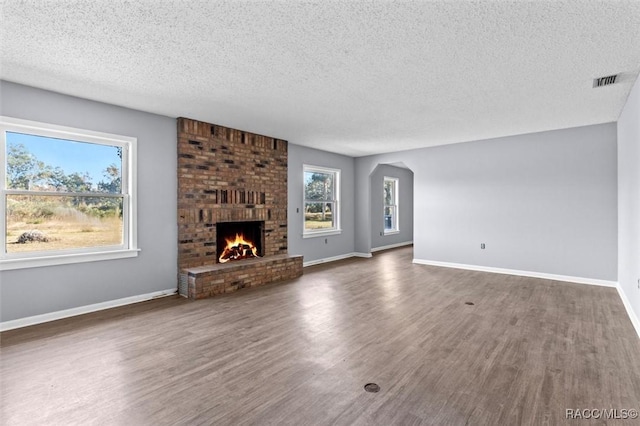 unfurnished living room featuring a healthy amount of sunlight, a textured ceiling, and dark wood-type flooring