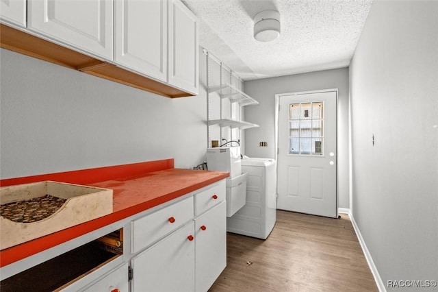 laundry area with light hardwood / wood-style floors, cabinets, separate washer and dryer, and a textured ceiling