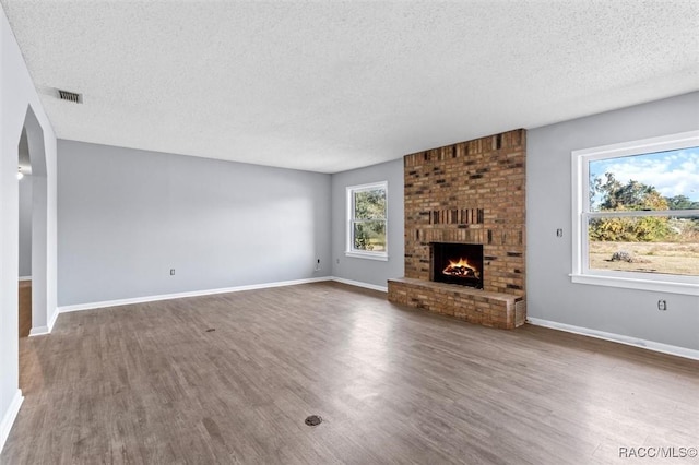 unfurnished living room featuring dark hardwood / wood-style flooring, a textured ceiling, and a brick fireplace