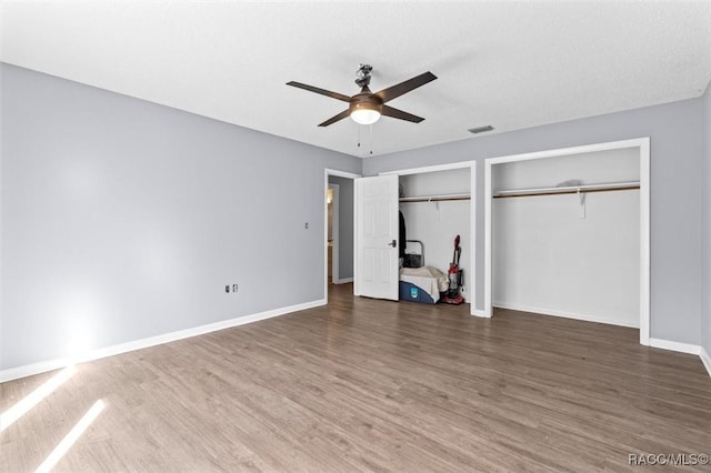 unfurnished bedroom featuring a textured ceiling, ceiling fan, dark wood-type flooring, and two closets