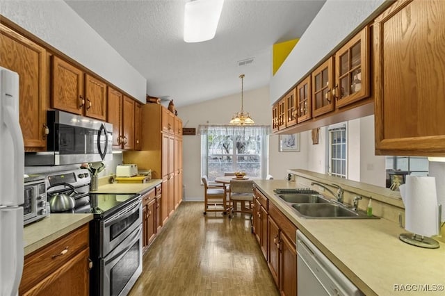 kitchen featuring stainless steel appliances, a sink, light countertops, brown cabinets, and decorative light fixtures