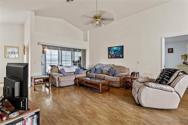 living room with a ceiling fan, light wood-type flooring, a wood stove, and high vaulted ceiling