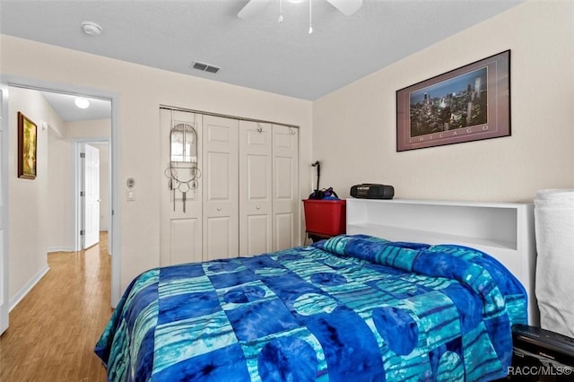 bedroom with a closet, visible vents, a ceiling fan, wood finished floors, and baseboards