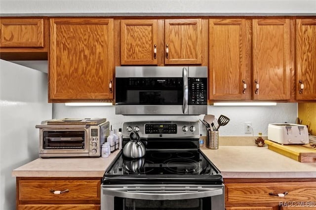 kitchen featuring light countertops, appliances with stainless steel finishes, brown cabinetry, and a toaster