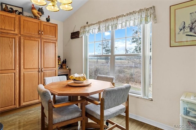 dining space featuring a chandelier, lofted ceiling, baseboards, and wood finished floors