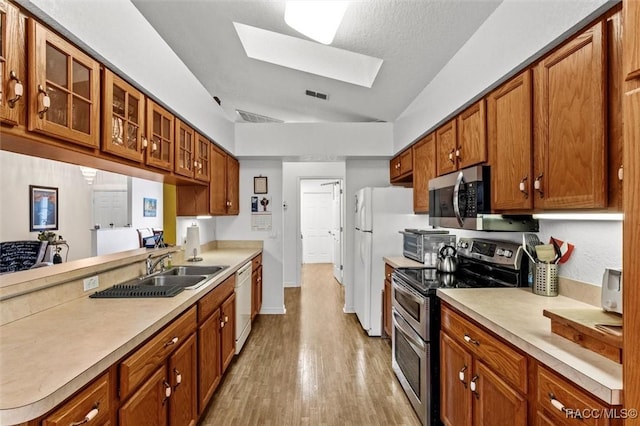 kitchen with light countertops, appliances with stainless steel finishes, glass insert cabinets, and brown cabinets