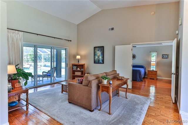 living room featuring high vaulted ceiling, baseboards, visible vents, and light wood finished floors