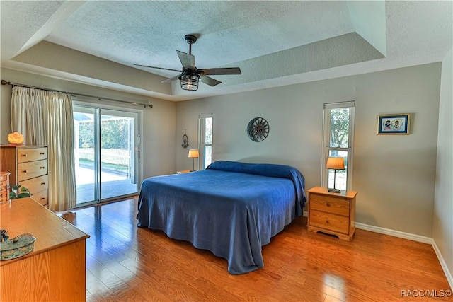 bedroom featuring access to exterior, light wood-style flooring, a tray ceiling, and baseboards