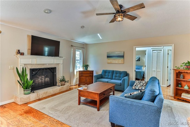 living area featuring ceiling fan, a fireplace, baseboards, and wood finished floors