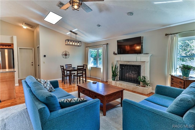 living area featuring light wood-style flooring, a premium fireplace, visible vents, and vaulted ceiling