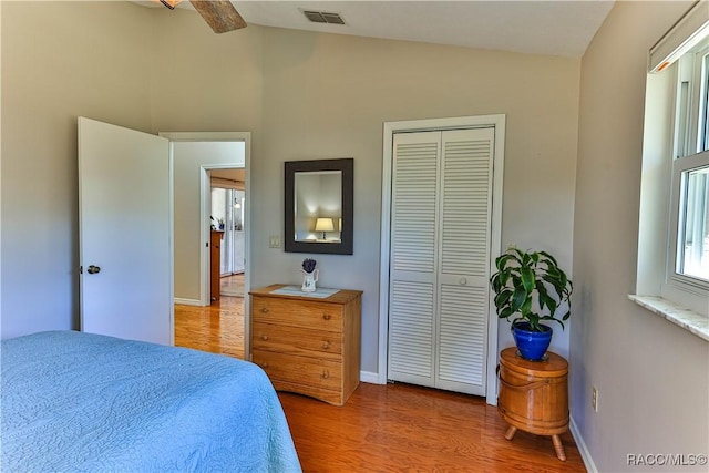 bedroom featuring light wood finished floors, a closet, visible vents, vaulted ceiling, and baseboards