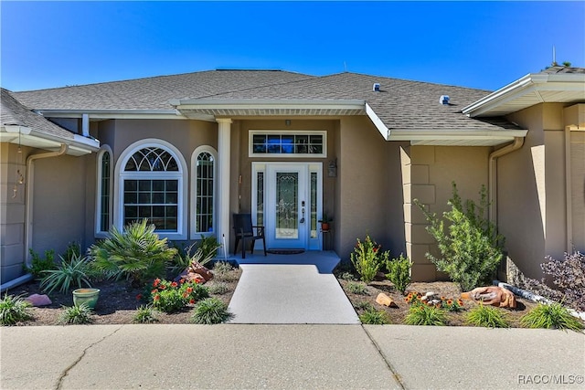 entrance to property featuring a shingled roof and stucco siding