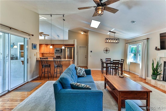 living room with a high end fireplace, ceiling fan, high vaulted ceiling, light wood-type flooring, and baseboards