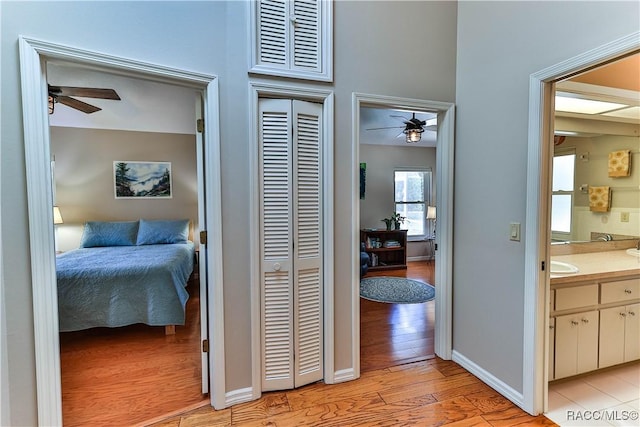 hall featuring baseboards, visible vents, a sink, and light wood finished floors