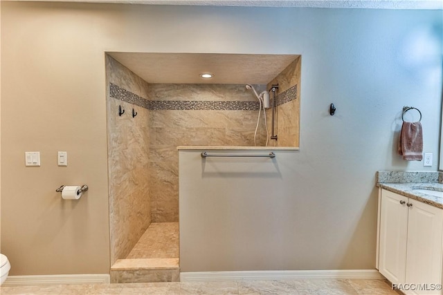 full bathroom featuring baseboards, a tile shower, vanity, and toilet