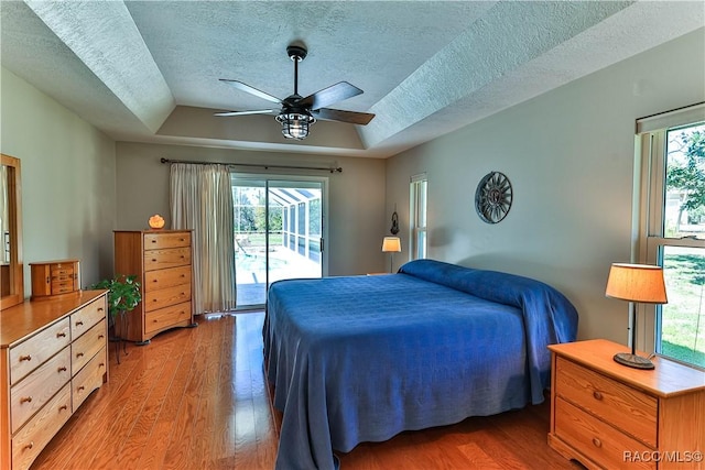 bedroom with a ceiling fan, access to exterior, a tray ceiling, a textured ceiling, and light wood-style floors