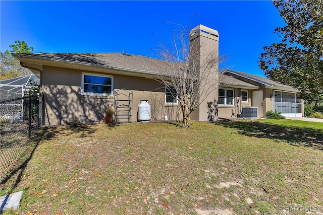 rear view of property with central AC unit, an attached garage, fence, a yard, and stucco siding