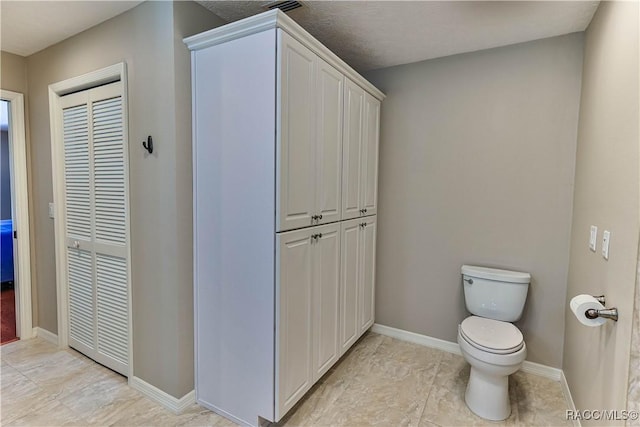 bathroom featuring a closet, toilet, and baseboards