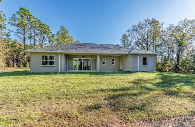 back of property with stucco siding, a ceiling fan, and a yard