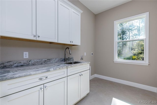 kitchen featuring white cabinets, light stone countertops, baseboards, and a sink